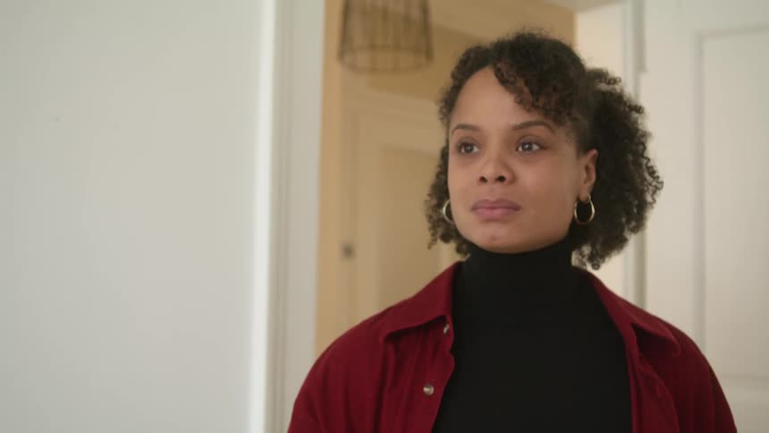A black woman crosses her arms and then looks downward and begins to cry