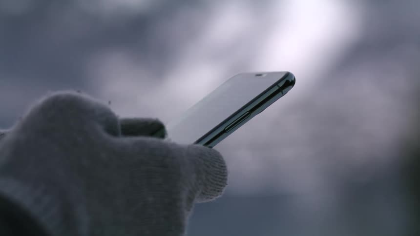 A person scrolling on a smartphone while wearing winter gloves