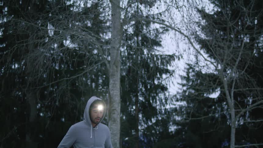 Man wearing a hoodie and a headlamp warming up in a snow covered forest