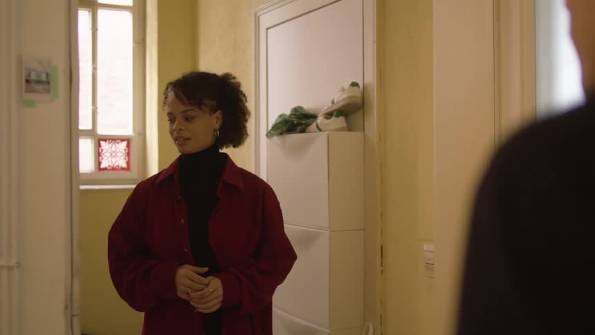 Man opens the door of his apartment to greet a woman wearing a red jacket