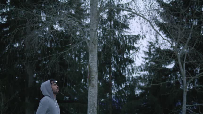 A man is jogging outdoors through a forest at dusk