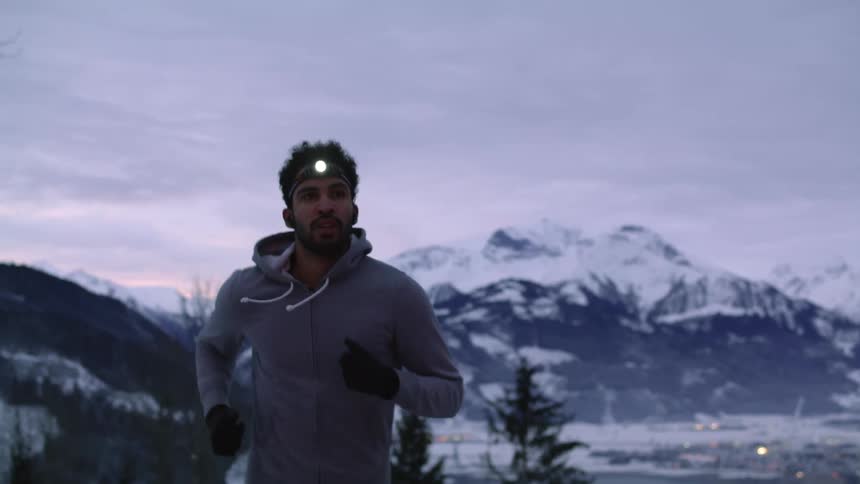 A man with a flashlight on his head runs along a mountain road on a cloudy evening
