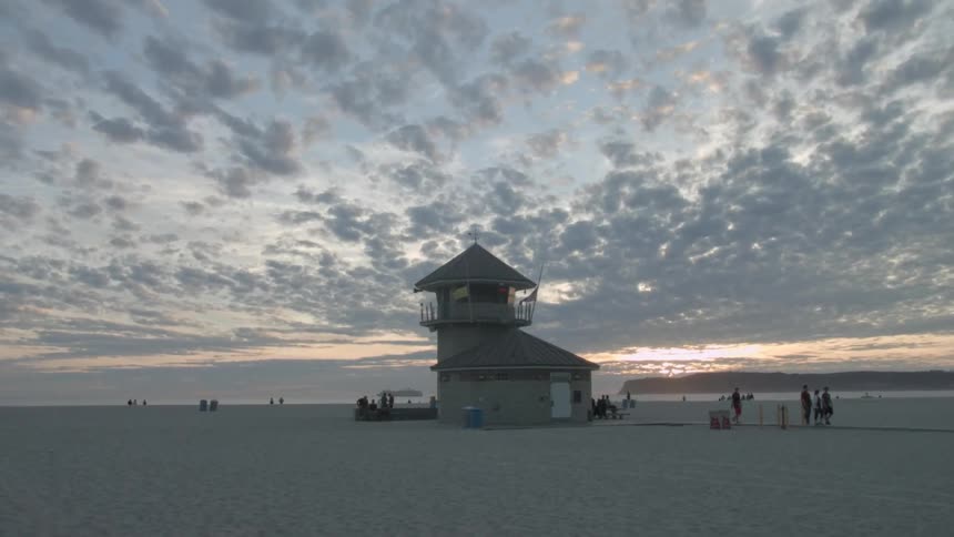 People walk along a beach at sunset