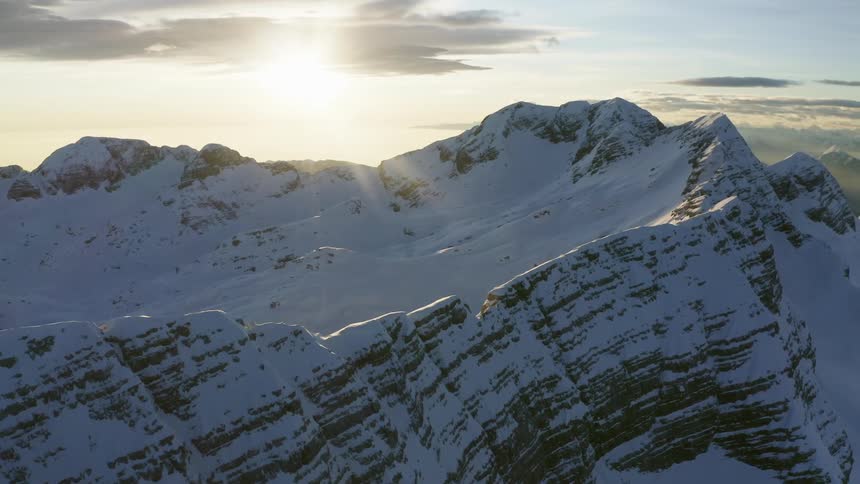 Snow covered mountain range with sun shining through the clouds