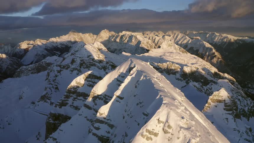 A mountain range covered in snow and ice with the sky and clouds in the background