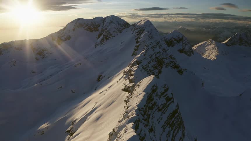 Snow covered mountain range with sun shining through the clouds