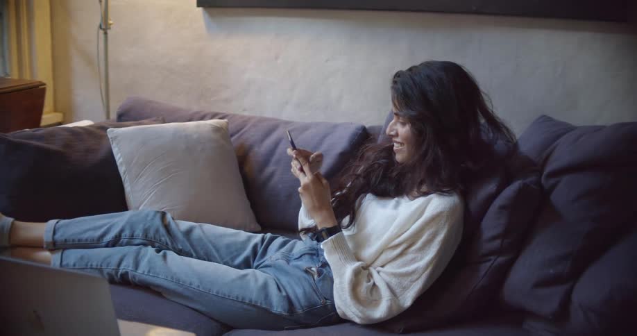 A woman in a room sitting on a couch using a smart phone