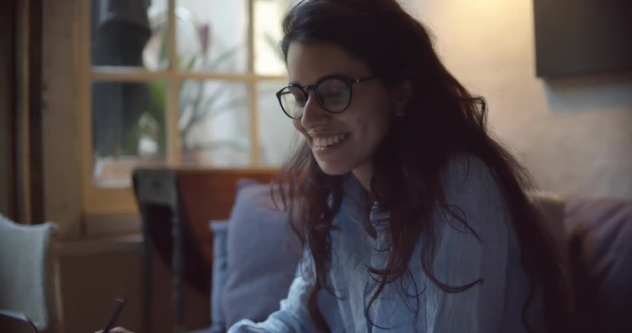 A woman in a room with glasses sitting on a couch next to a laptop