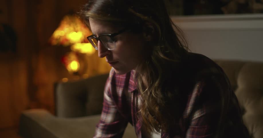 A woman with glasses in a room sitting on a couch with a lamp in the background