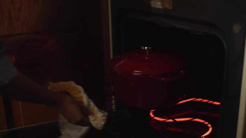 Young woman opens a hot electric oven to take out a cooking pot