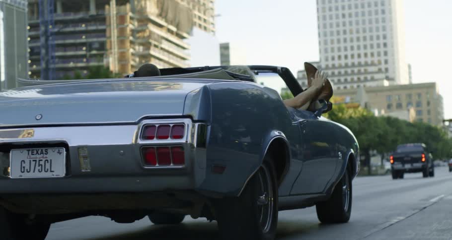 Two people driving down the road in a convertible