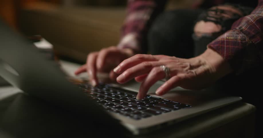 A person sitting down on a couch indoors types on a laptop computer