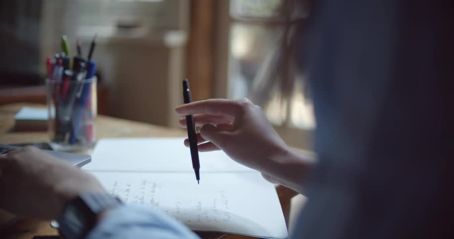 Woman sitting in front of a notebook spins a pen on her fingers