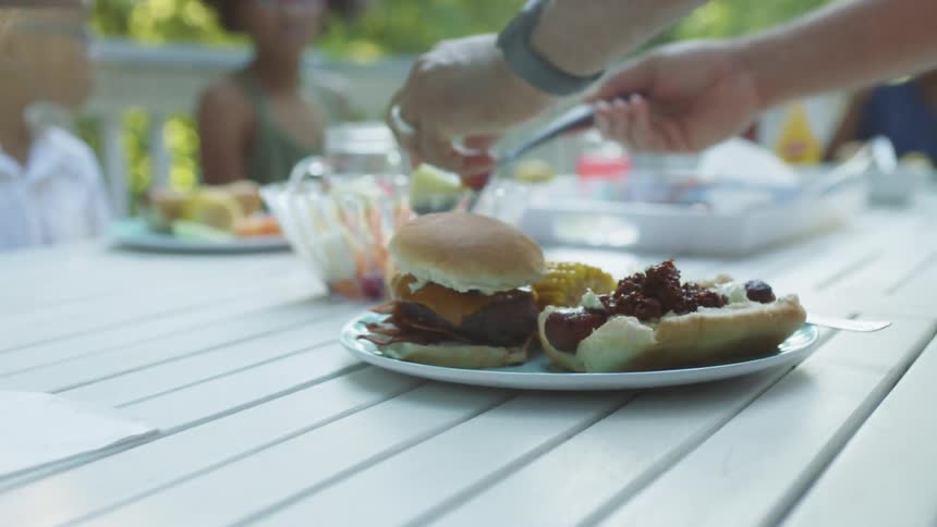 Family sitting at a table in the patio ready to eat hamburgers and hot dogs