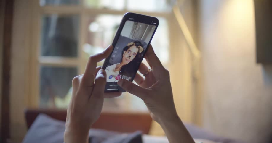 Woman resting on a couch at home applies filters to a selfie taken with her smartphone