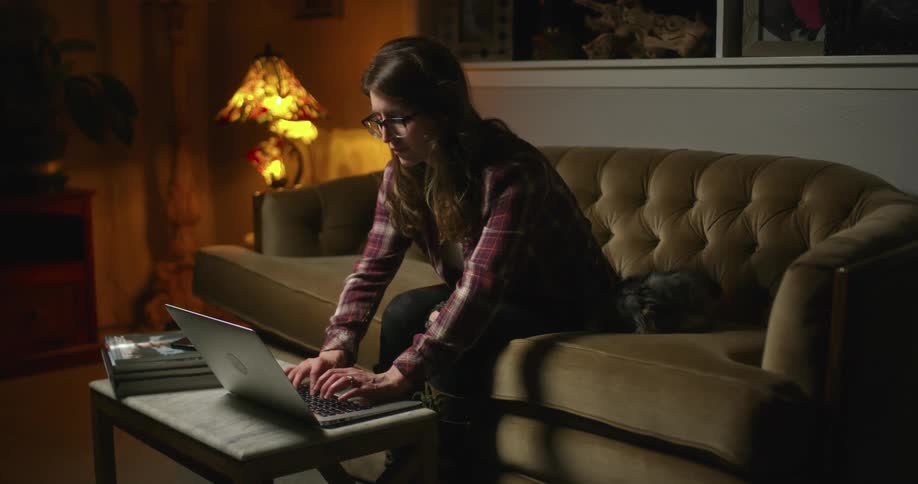 A woman sitting on a couch typing on a laptop