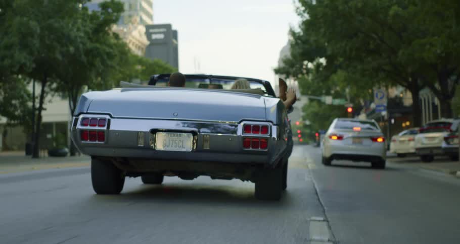Two texans driving down a city street in a convertible