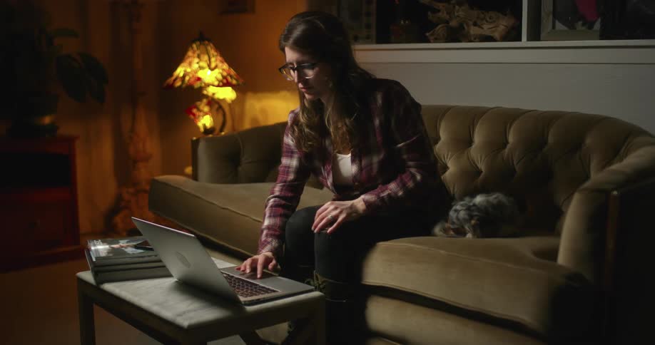 A woman is sitting indoors and looking at a laptop