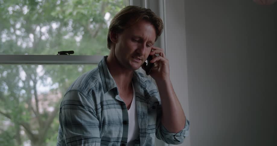 A man smiling and laughing while talking on a cell phone next to a window