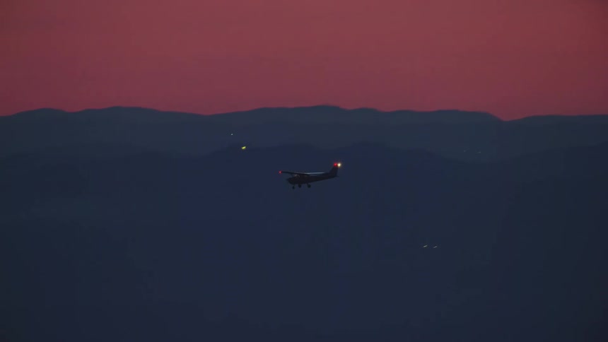A small single engine white airplane flies in beautiful blue hour magic light in this air to air aerial under a pink sunset sunrise sky