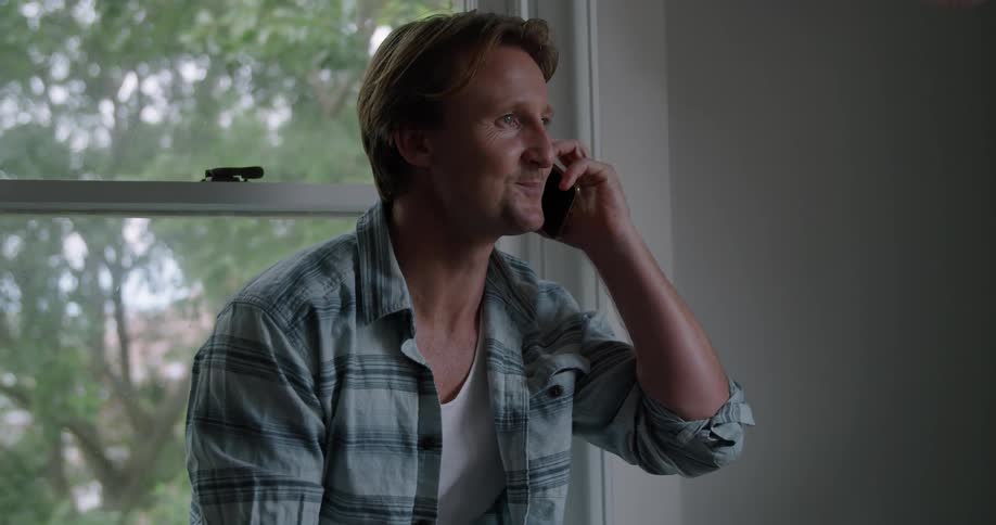 Man happily answers a call on his smartphone in a room