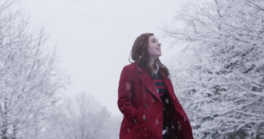A woman wearing a red jacket jumps as it snows