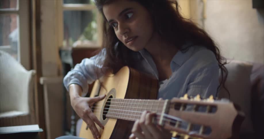 A woman sits at home and practices playing the guitar