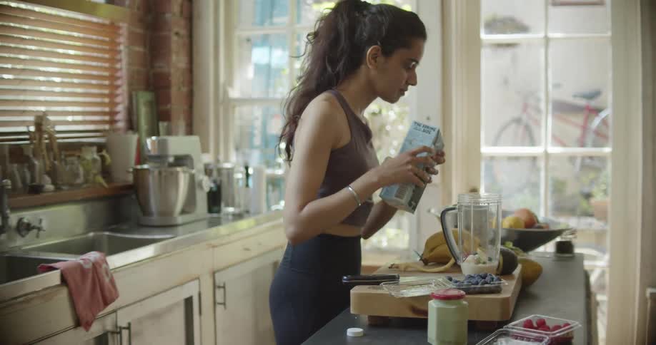 A woman in the kitchen pouring milk into a blender with a door in the background