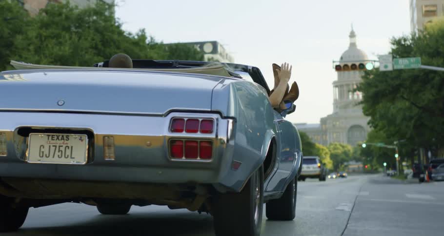 A man and a woman driving in a convertible on a city street