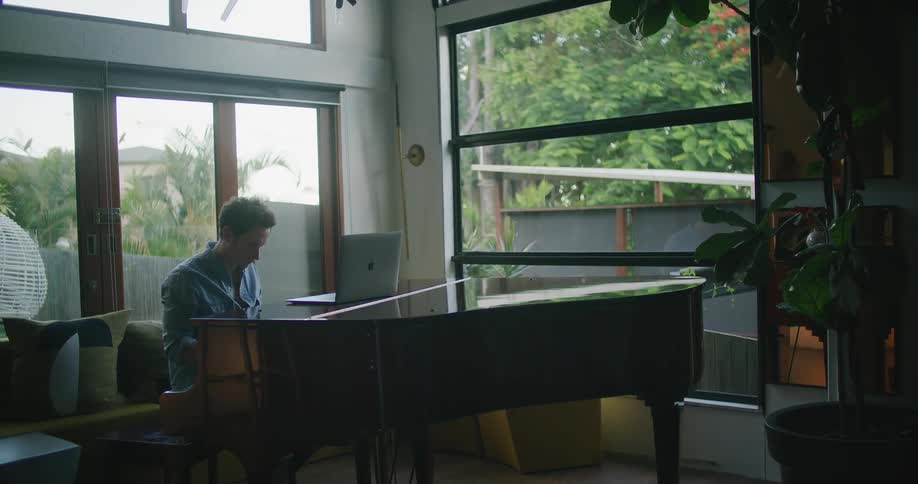 A man composing musing while playing piano in the living room at home