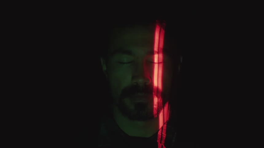 A red light strip scans across a mans face in a dark place