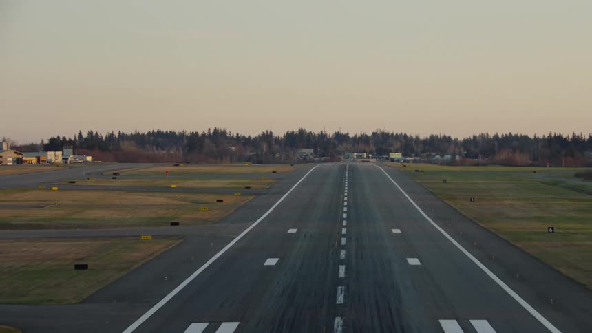 Landing airplane POV aerial shot of a large commercial landing runway with green grass and trees and hills in the background. Perfect shot to simulate take off or if reversed, landing