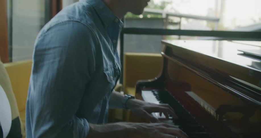 A man reading music sheets on a laptop while playing piano at home