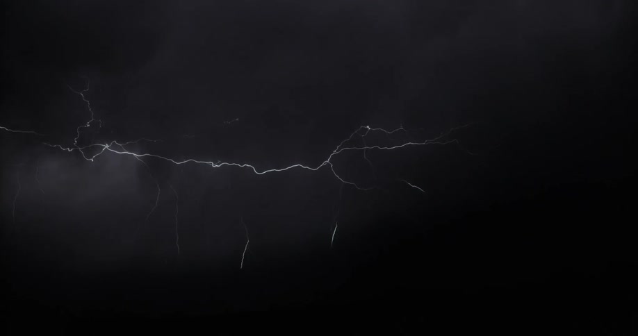Lightning strikes across clouds in a thunderstorm in a dark sky at nighttime