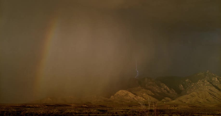 A rainbow in front of rainclouds with lightning flashing in the sky