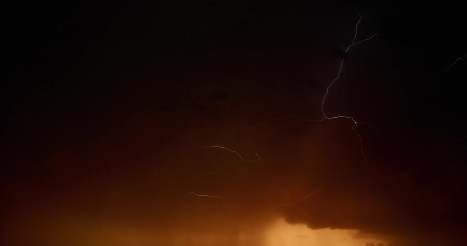 Lightning bolts flash and branch out under a dark storm cloud in a dark orange sky