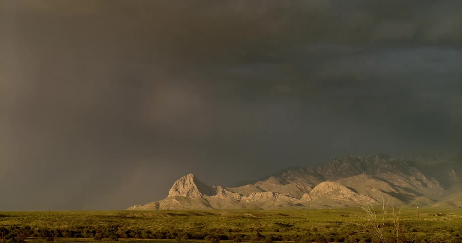 Lightning bolts flash from a dark sky over a mountain range