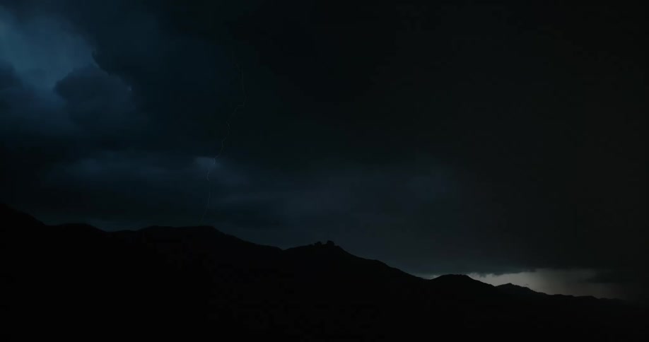 Lightning bolts flash in a dark sky and come down near a mountain