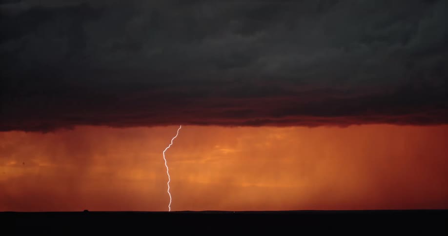 Lightning flashing in a cloudy orange sky during a thunderstorm