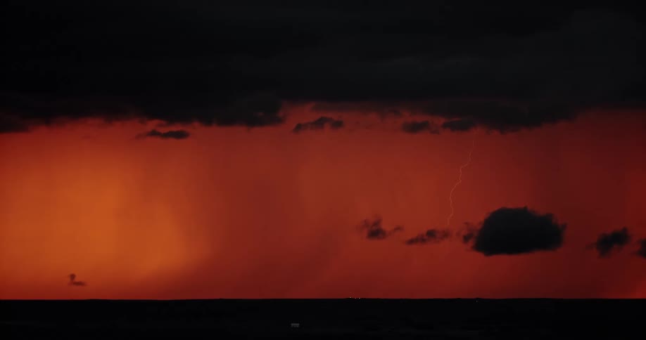 Lightning streaking arcs flashing over the silhouette of black clouds on a red sky