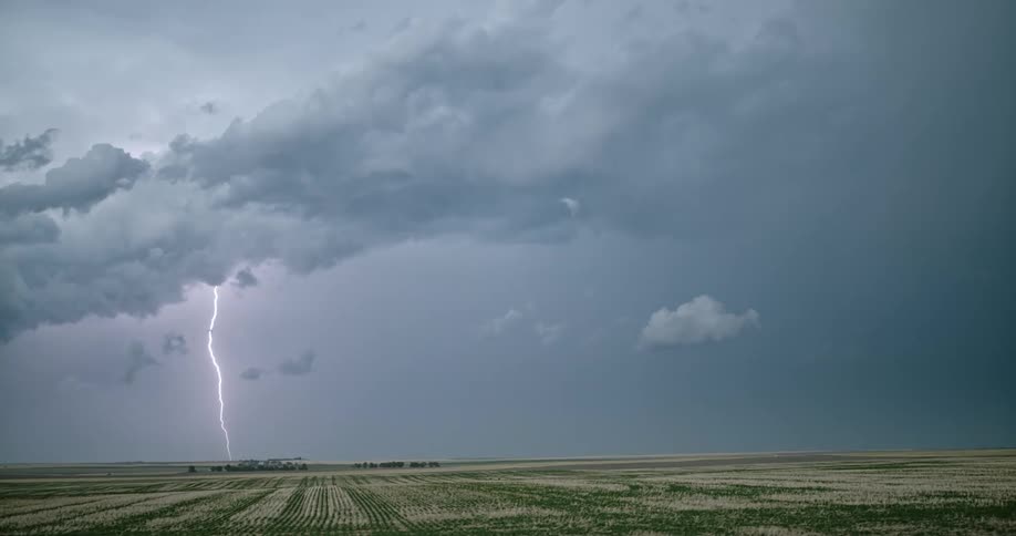 Lightning flashes from storm clouds in the sky over farmland
