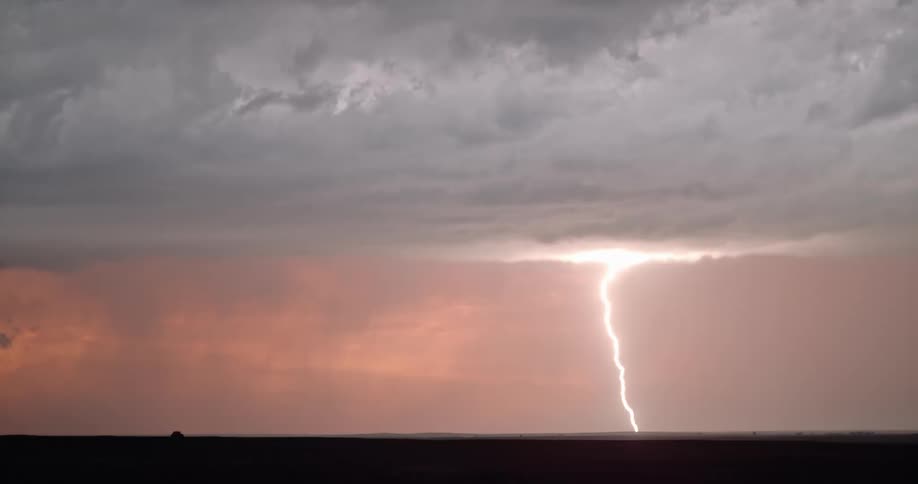 Lightning streaking arcs flashing over the silhouette of black clouds on a red sky