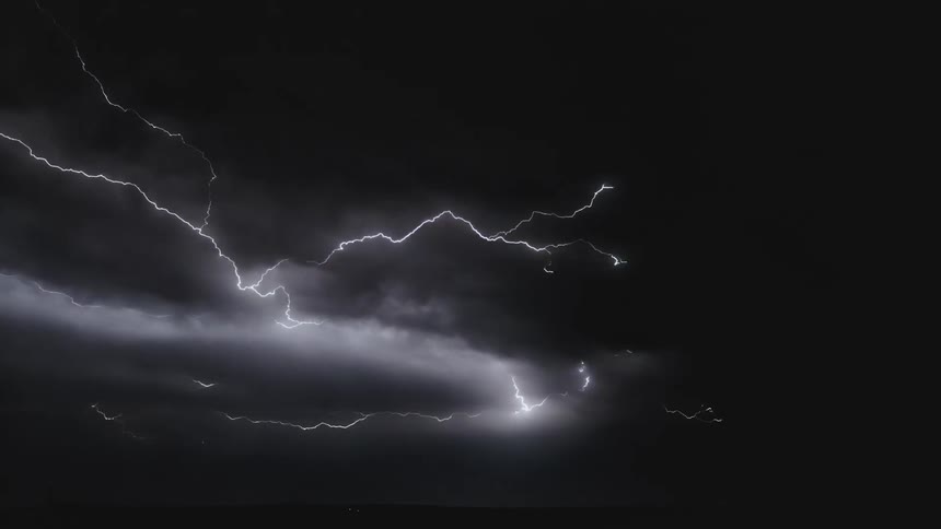 Lightning flashes and scatters across dark clouds in the sky in a thunderstorm at nighttime