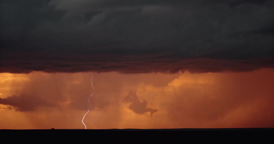 Clouds scattered about in an orange sky at sunset with lightning striking the ground