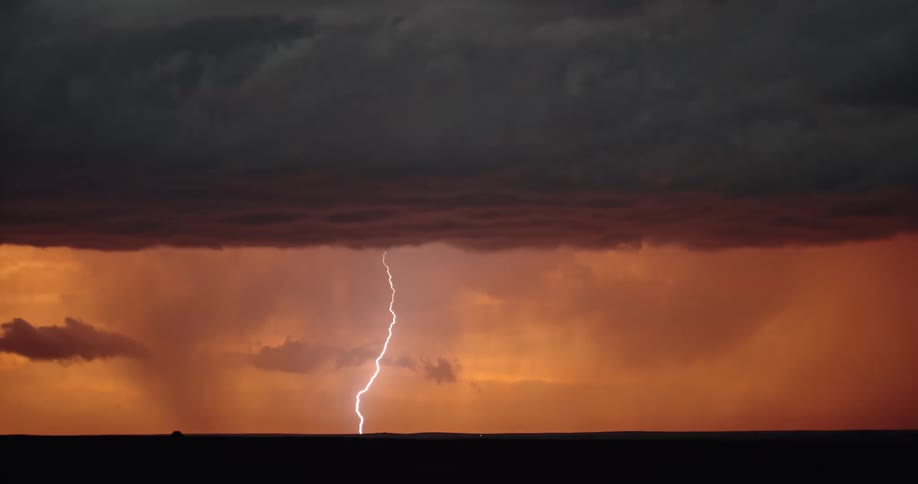 Lightning strikes down in the distance from a large set of storm clouds in the evening