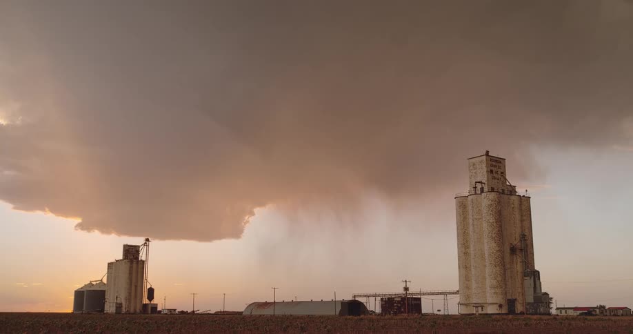 Lightning streaking arcs flashing across yellow storm clouds hitting the ground over the grain silos on a field