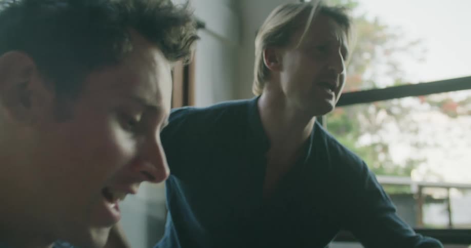 A man leans against a piano singing along with his friend who is playing