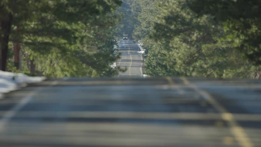 Looking back at a car cresting a rolling hill on a rural highway on a sunny day in the winter as the scene is obscured by another rolling hill and painted yellow lines