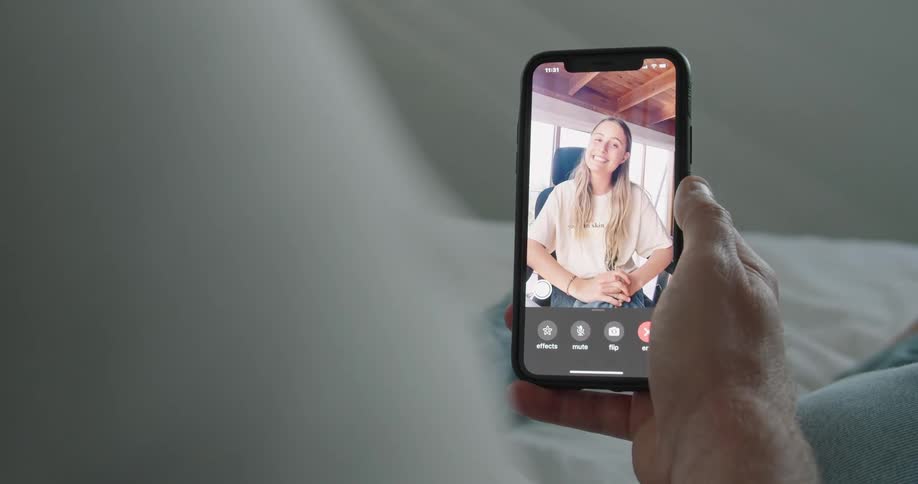 A person in a bedroom laying on a bed with sheets holding a smart phone