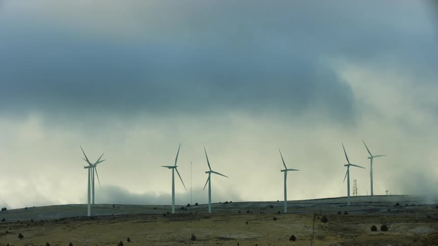 Wind turbines rotate lazily on a high ridge at sunset during a frigid winter storm that creates low altitude clouds